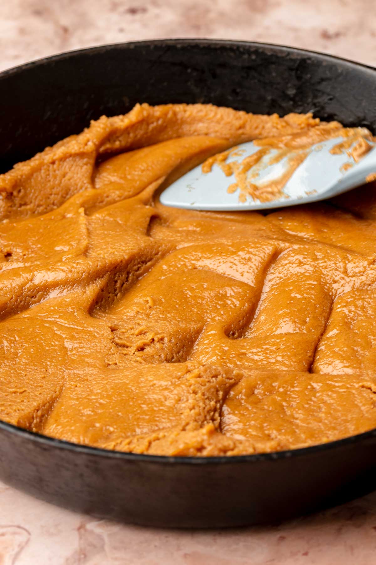 A spatula presses cookie butter batter into a skillet.