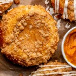 Baked pumpkin brioche buns on parchment paper with a bowl of pumpkin next to them.