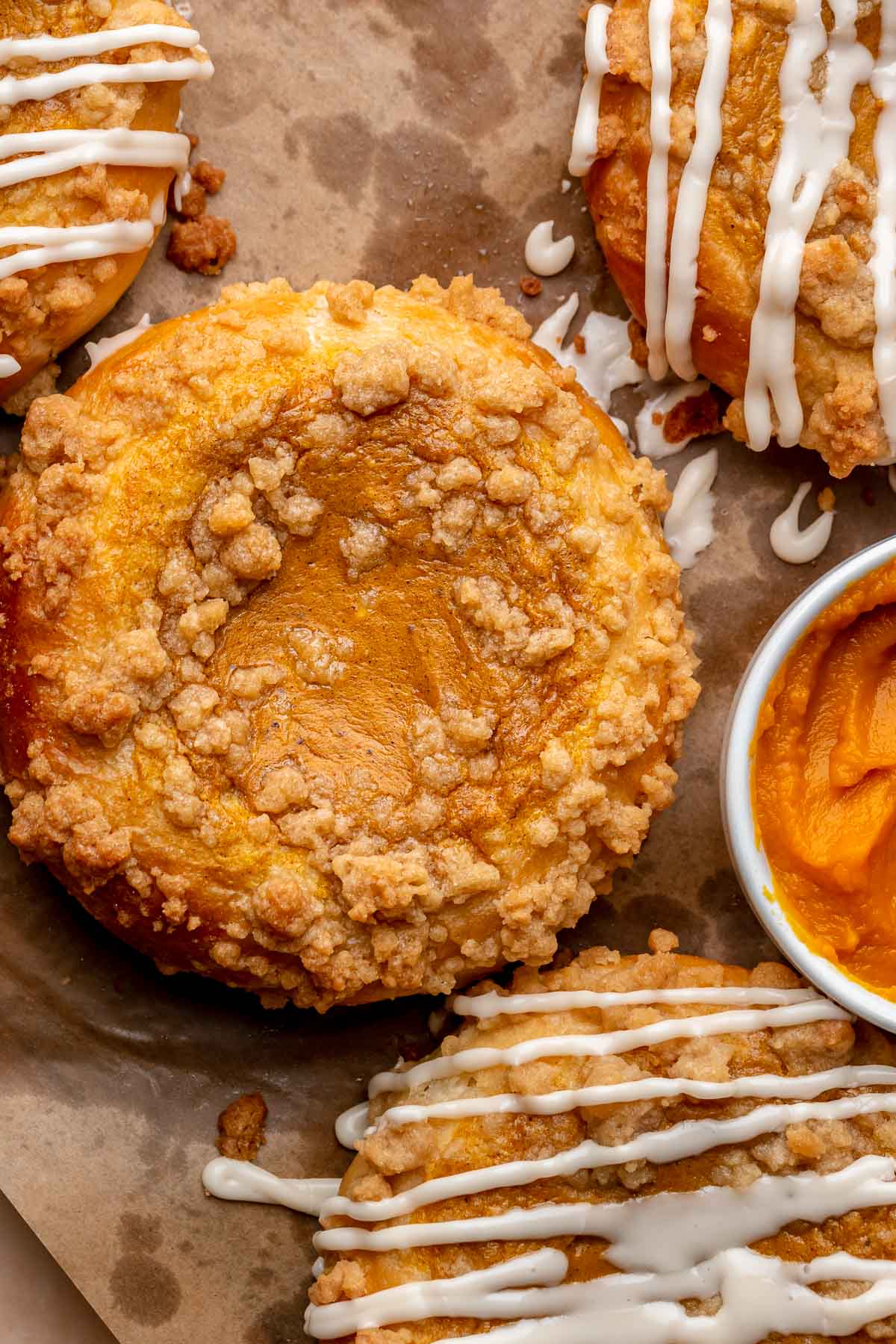 Baked pumpkin brioche buns on parchment paper with a bowl of pumpkin next to them.