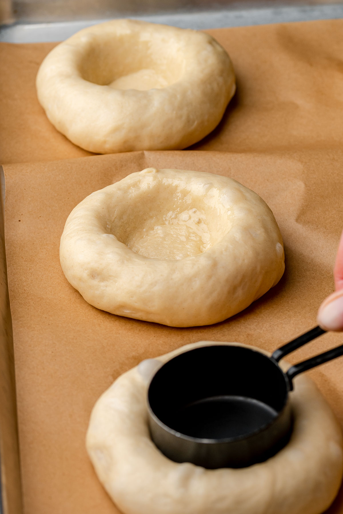 A hand presses a measuing cup into a ball of dough to make an indent.