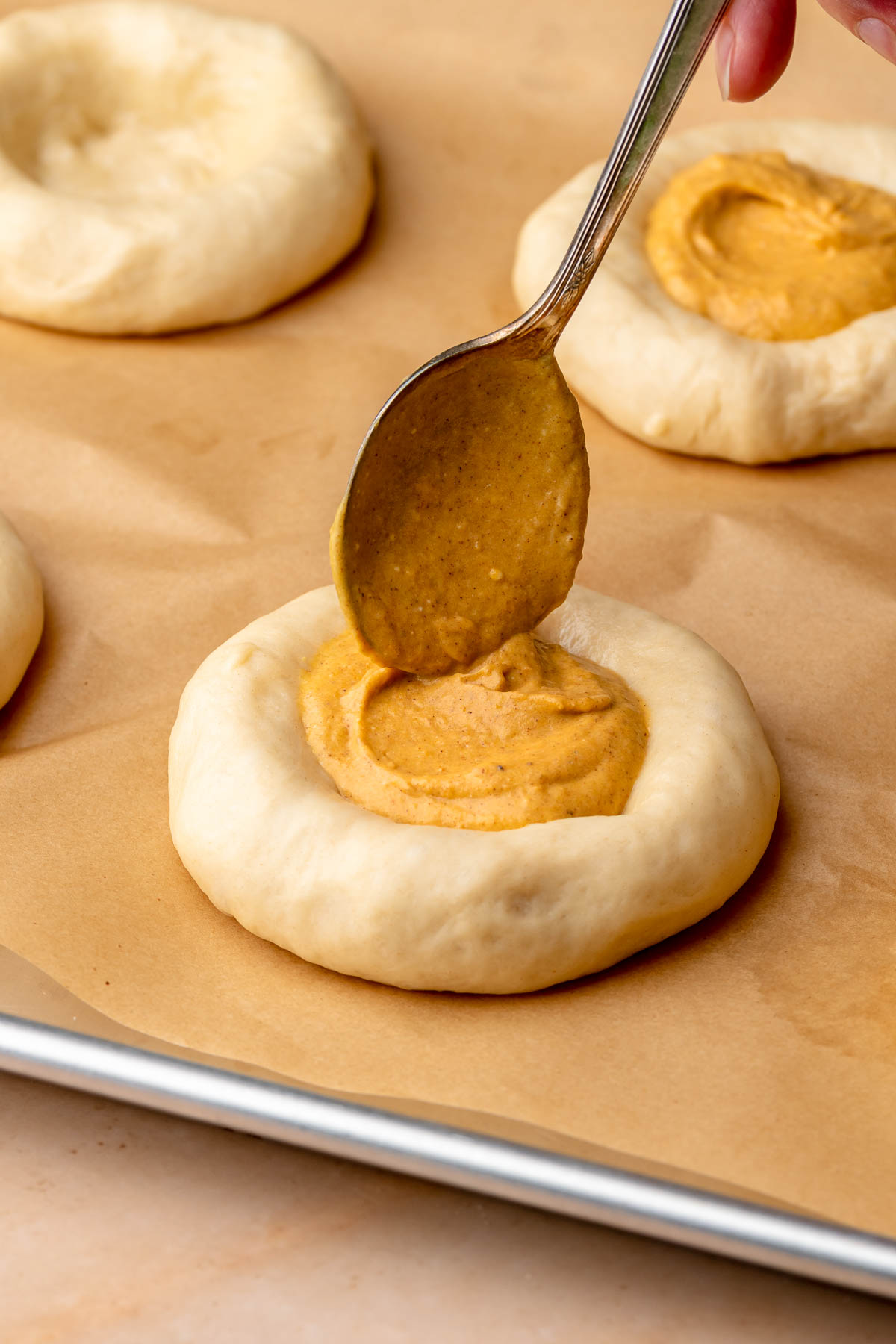 A spoon adds pumpkin cream cheese filling to the brioche dough.