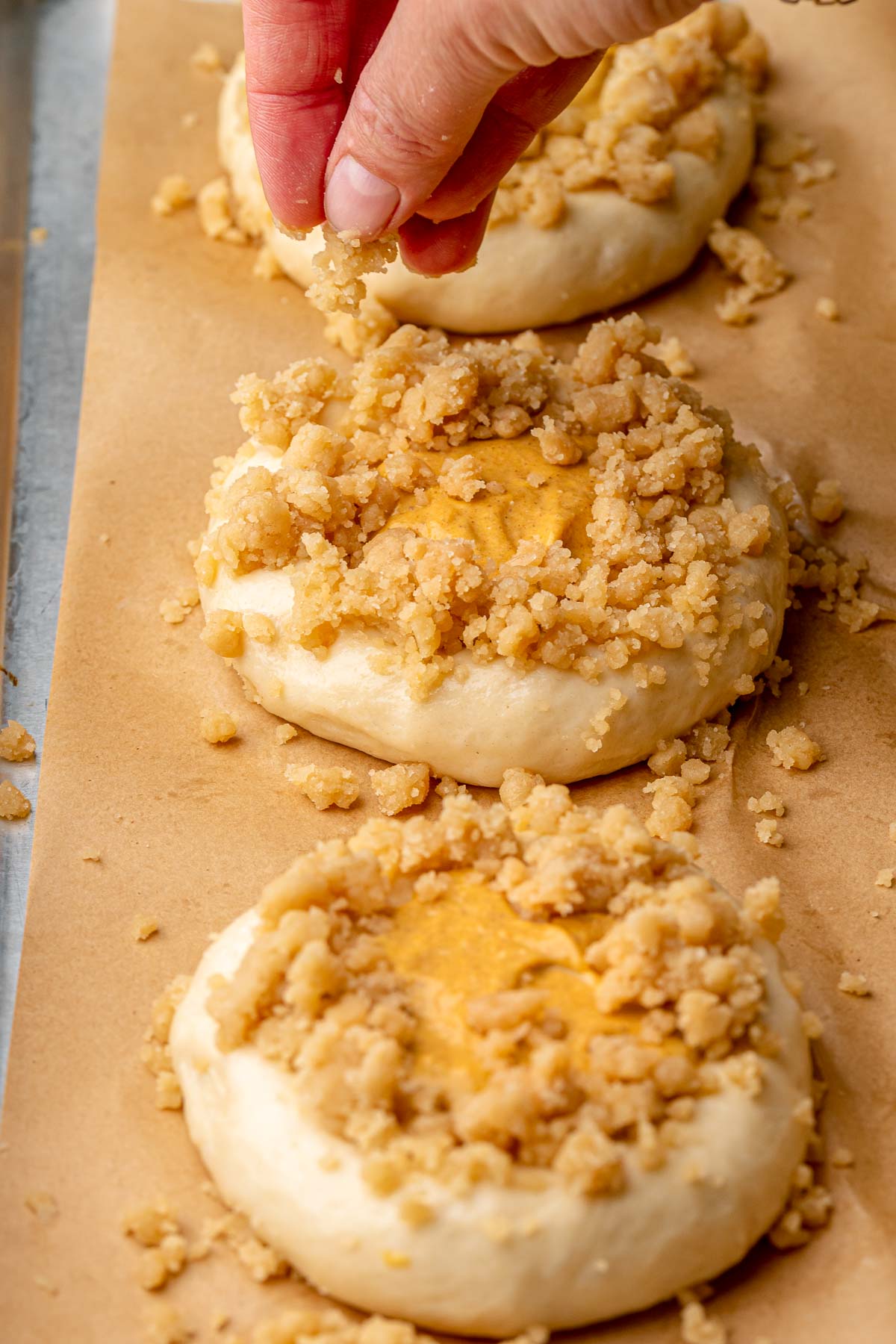 A hand adds crumble topping to the top and sides of the brioche buns.