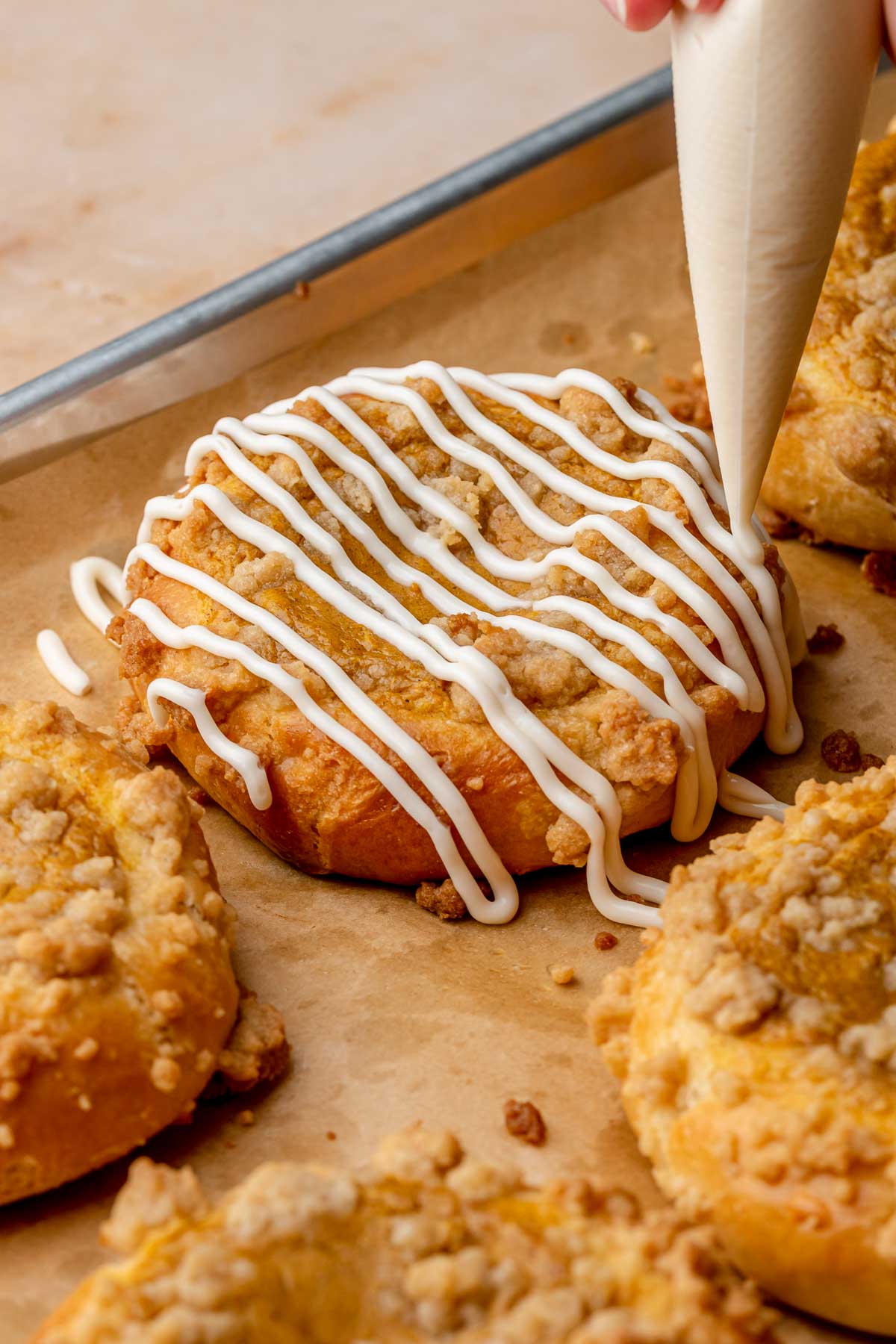 A piping bag adds vanilla glaze to a baked pumpkin brioche bun.