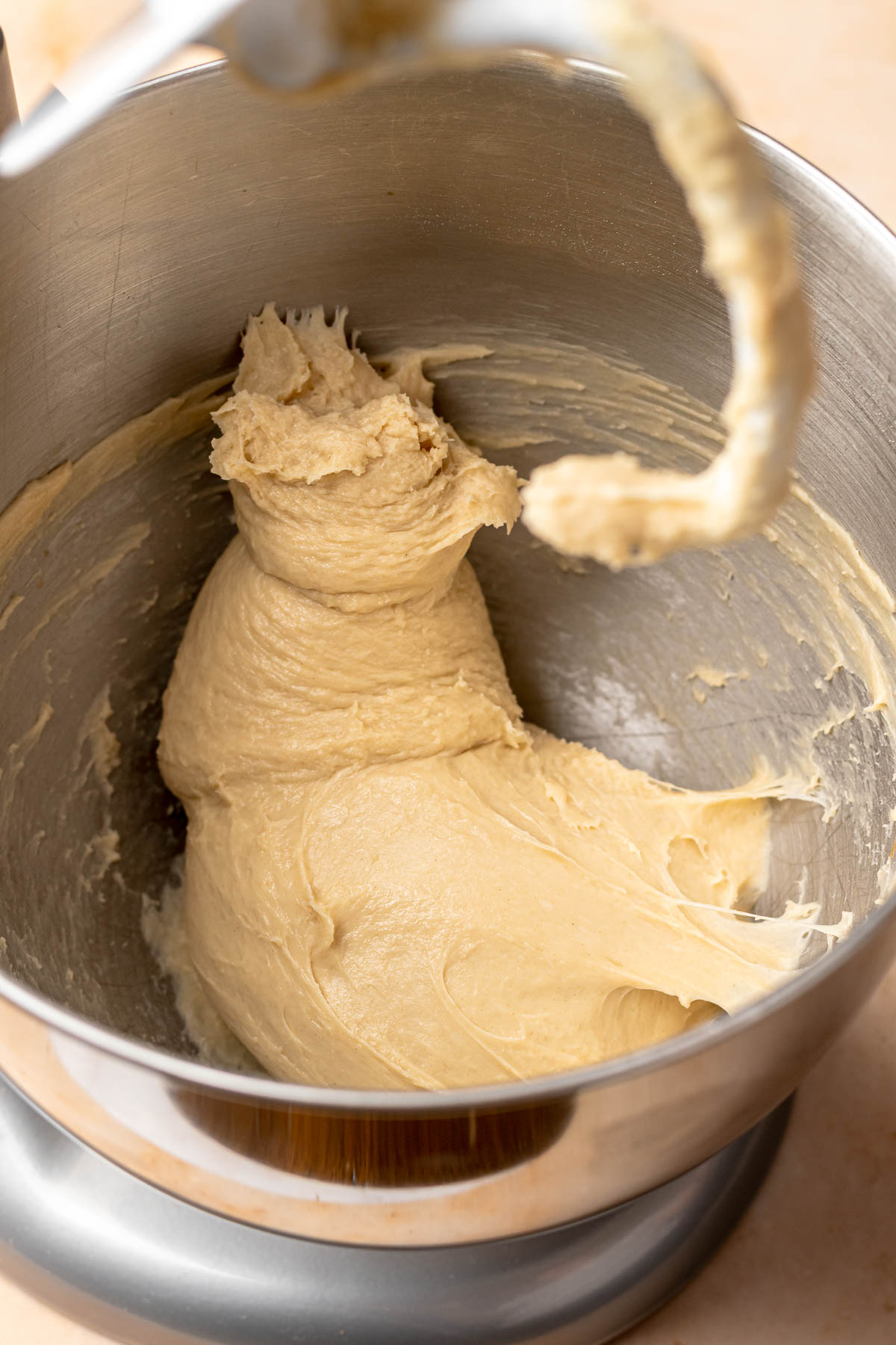 A bowl and dough hook with mixed dough in it.