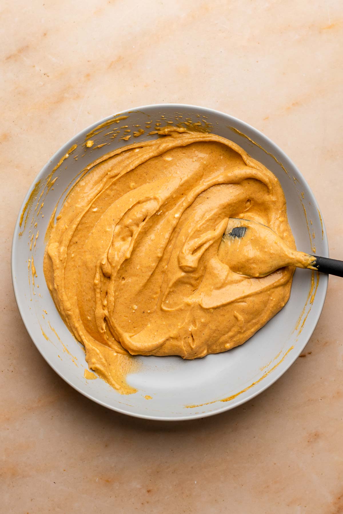 A spatula sits in a bowl of pumpkin cream cheese filling.