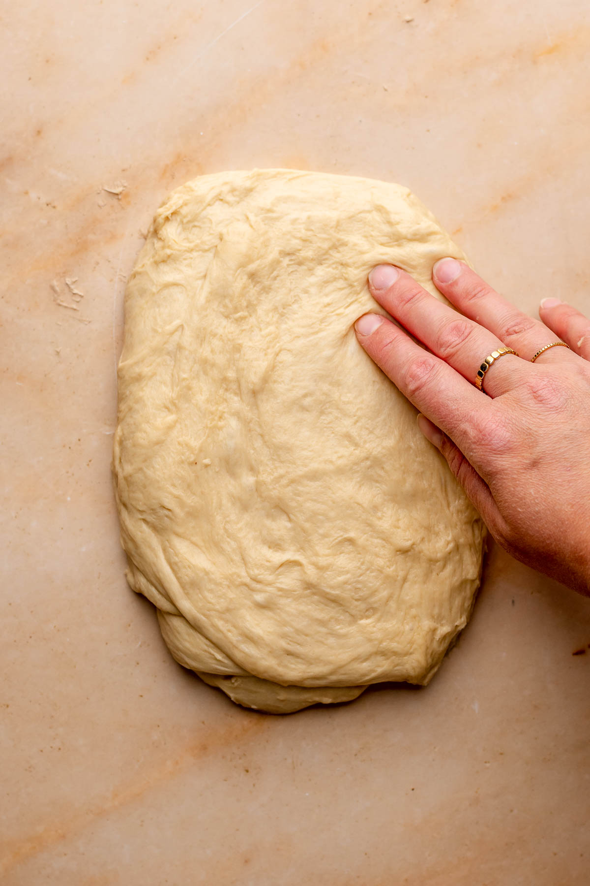 A hand presses brioche dough into a rectangle on a counter.