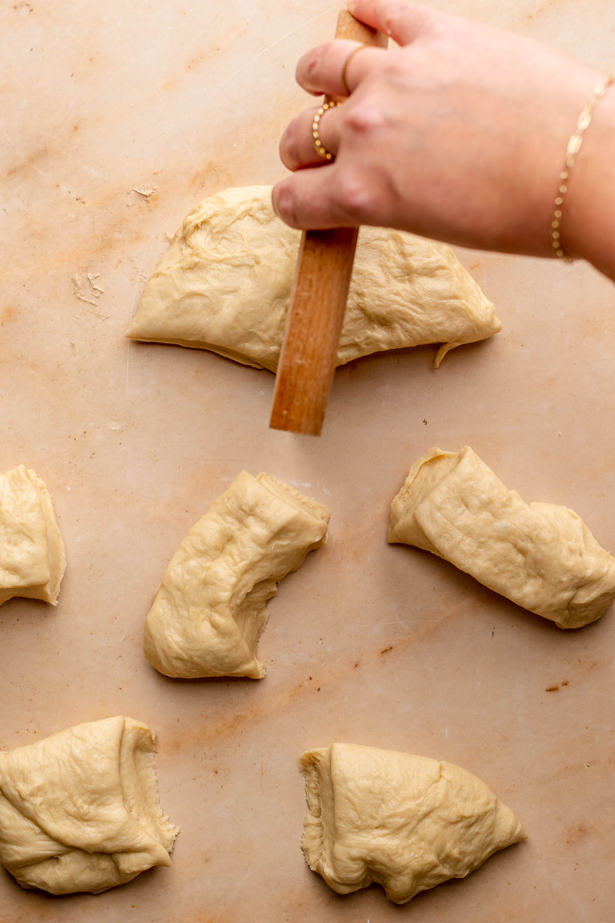 A hand uses a bench scraper to cut dough into pieces.