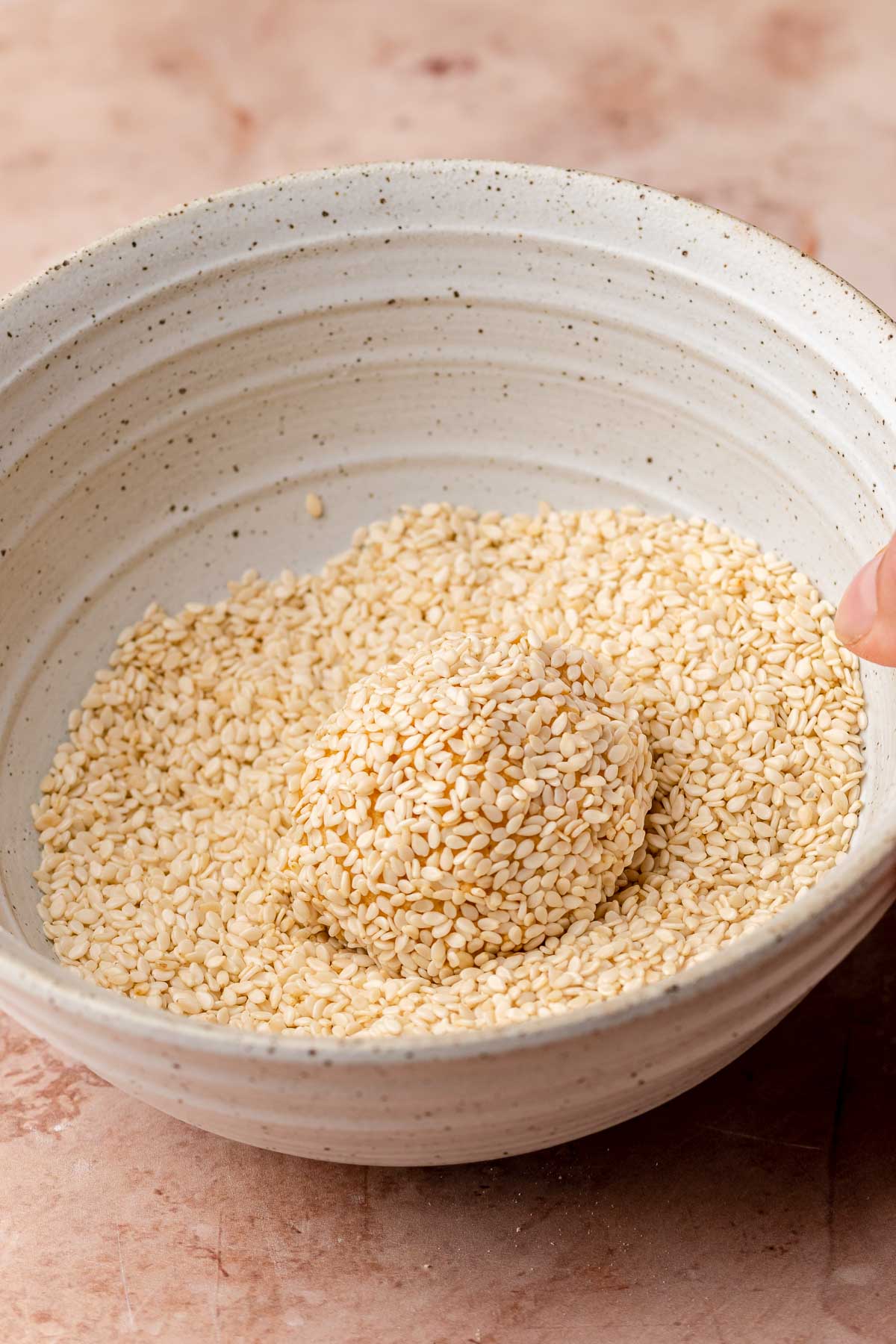 Sweet potato cookie dough balls in a bowl of sesame seeds.