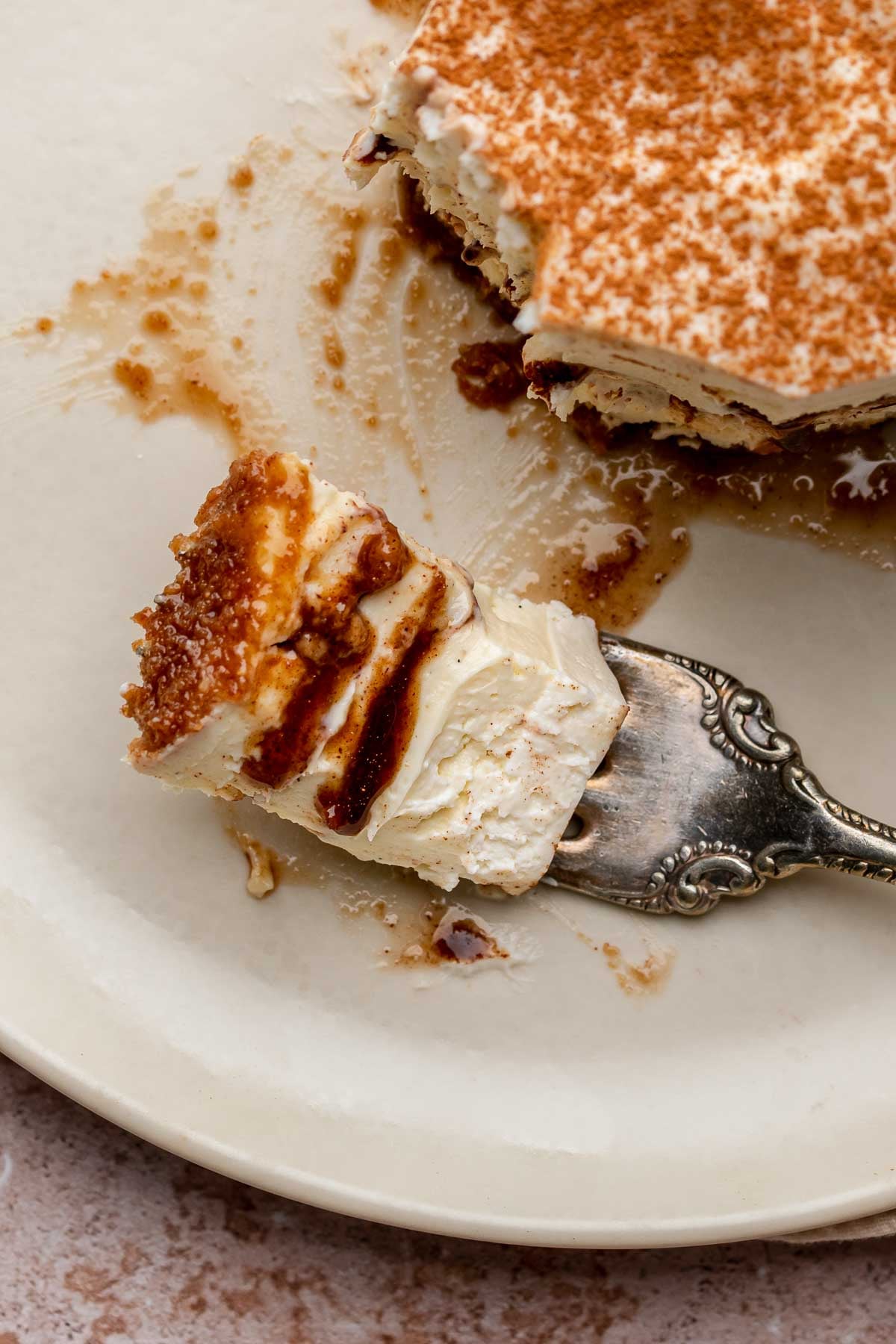 A fork holds a piece of cinnamon roll cheesecake on a plate.