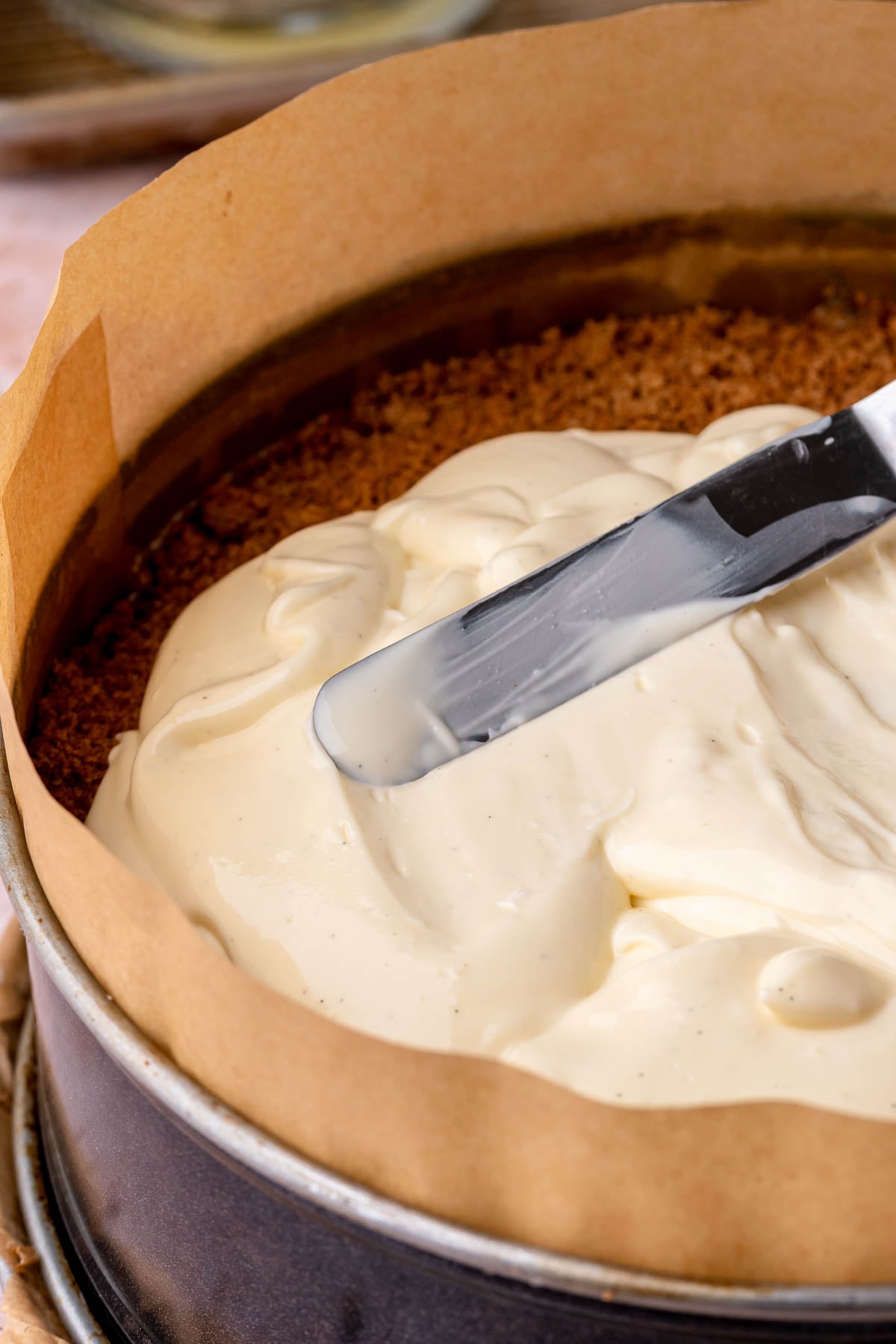 A spatula spreads cheesecake batter into crust.
