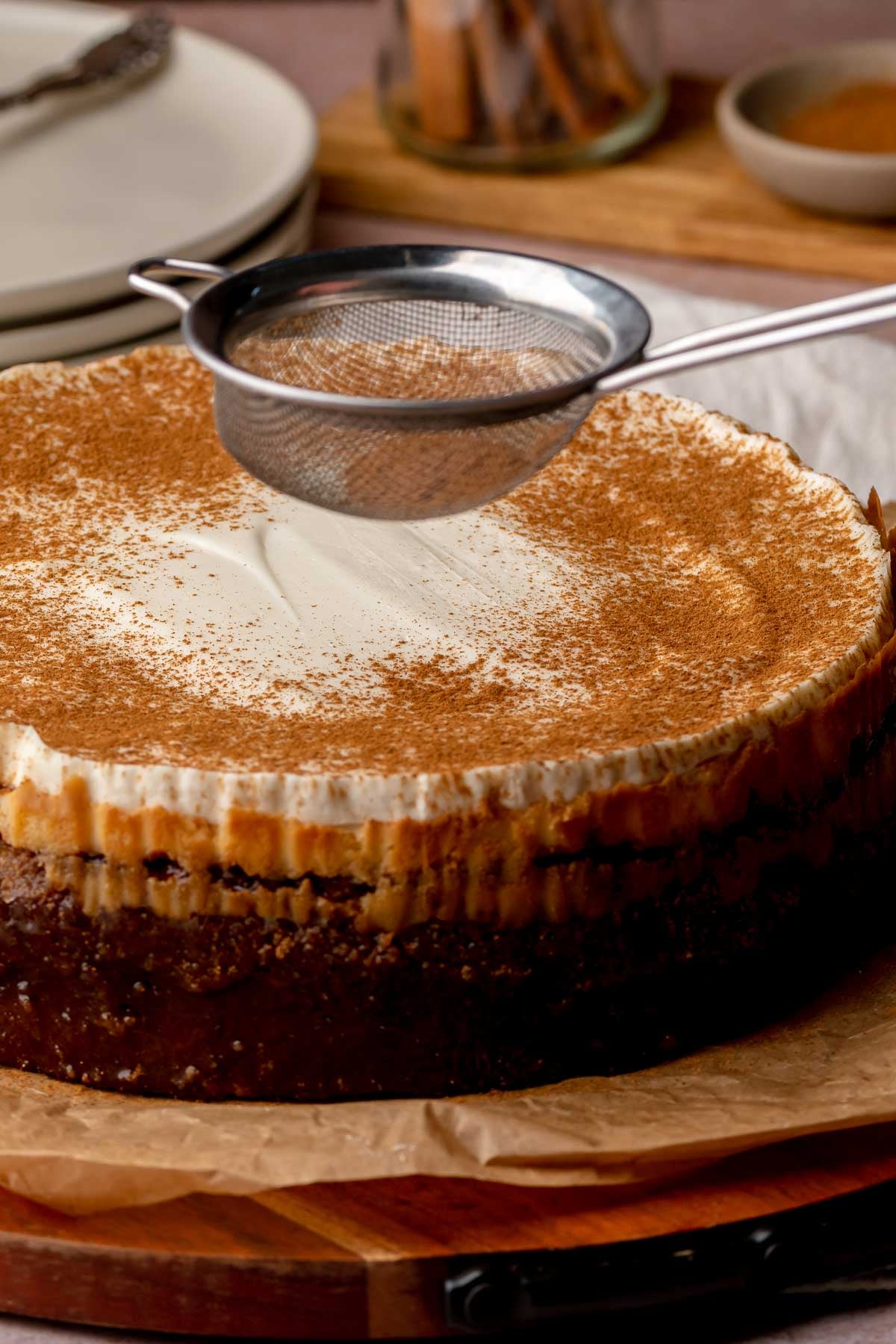 A sieve dusts cinnamon onto a baked cheesecake.