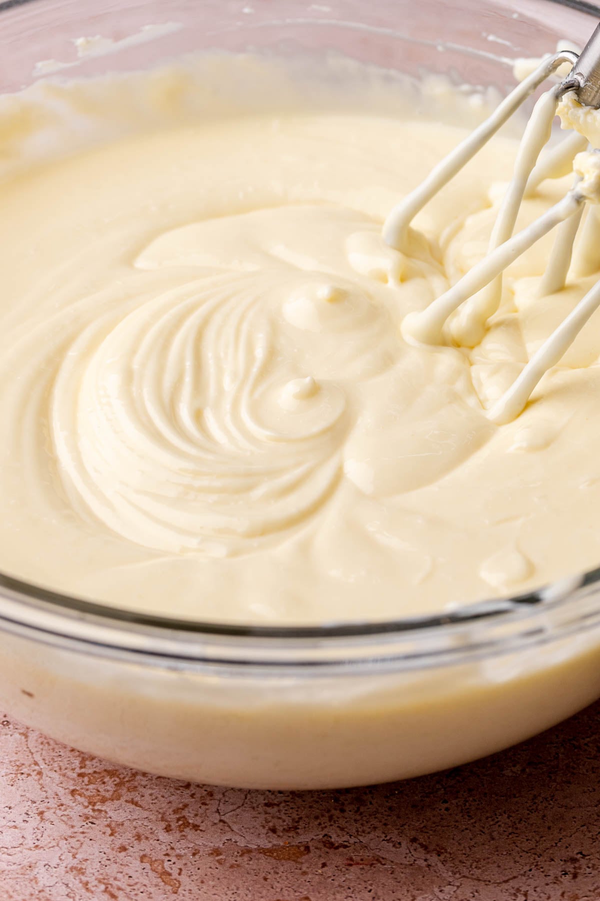 Beaters mixing cheesecake batter in a bowl.