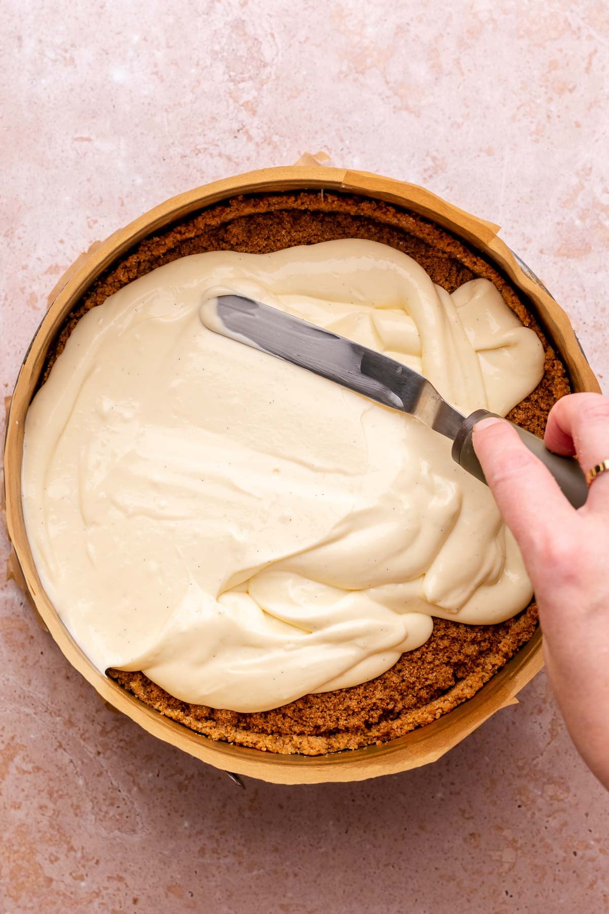 A spatula spreads cheesecake batter into crust.
