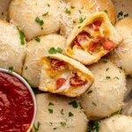 Pizza bites in a baking dish with marinara on the side. One is broken open.