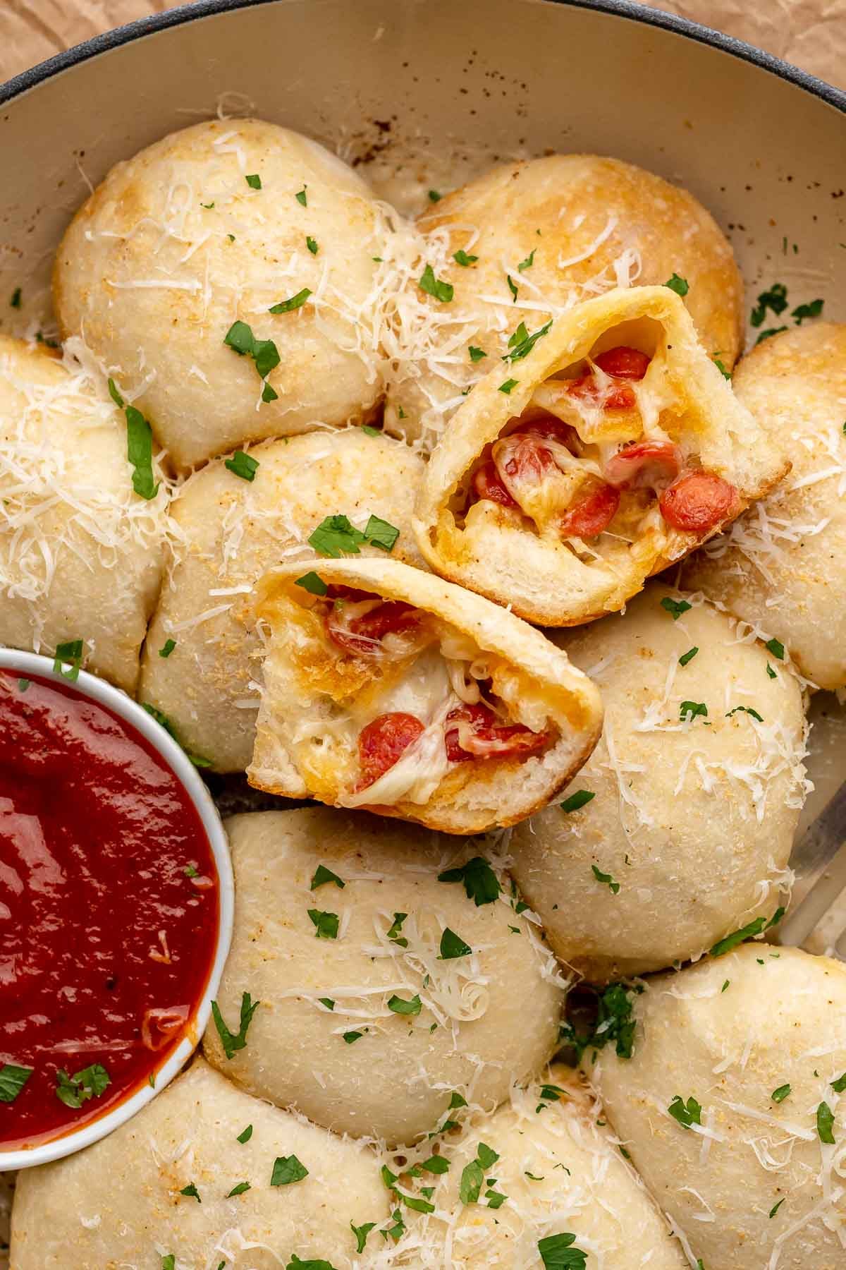 Pizza bites in a baking dish with marinara on the side. One is broken open.