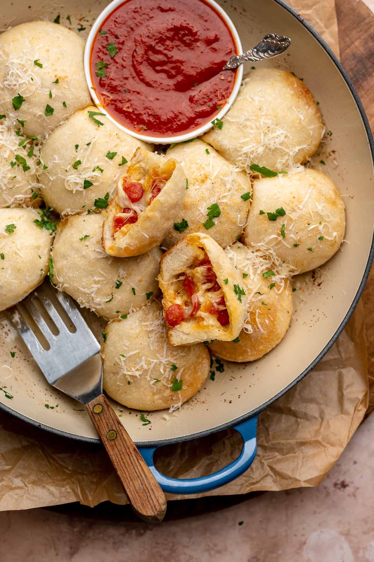 Pizza bites in a baking dish with marinara on the side. One is broken open.