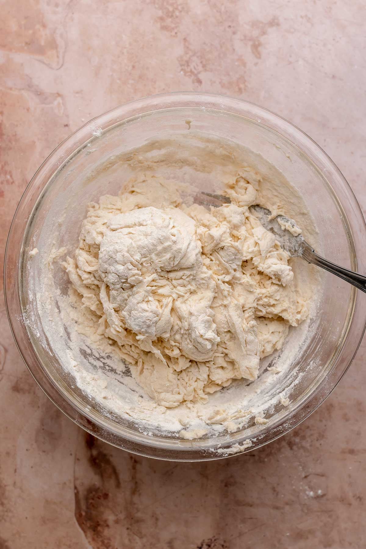 A fork mixes pizza dough in a bowl.