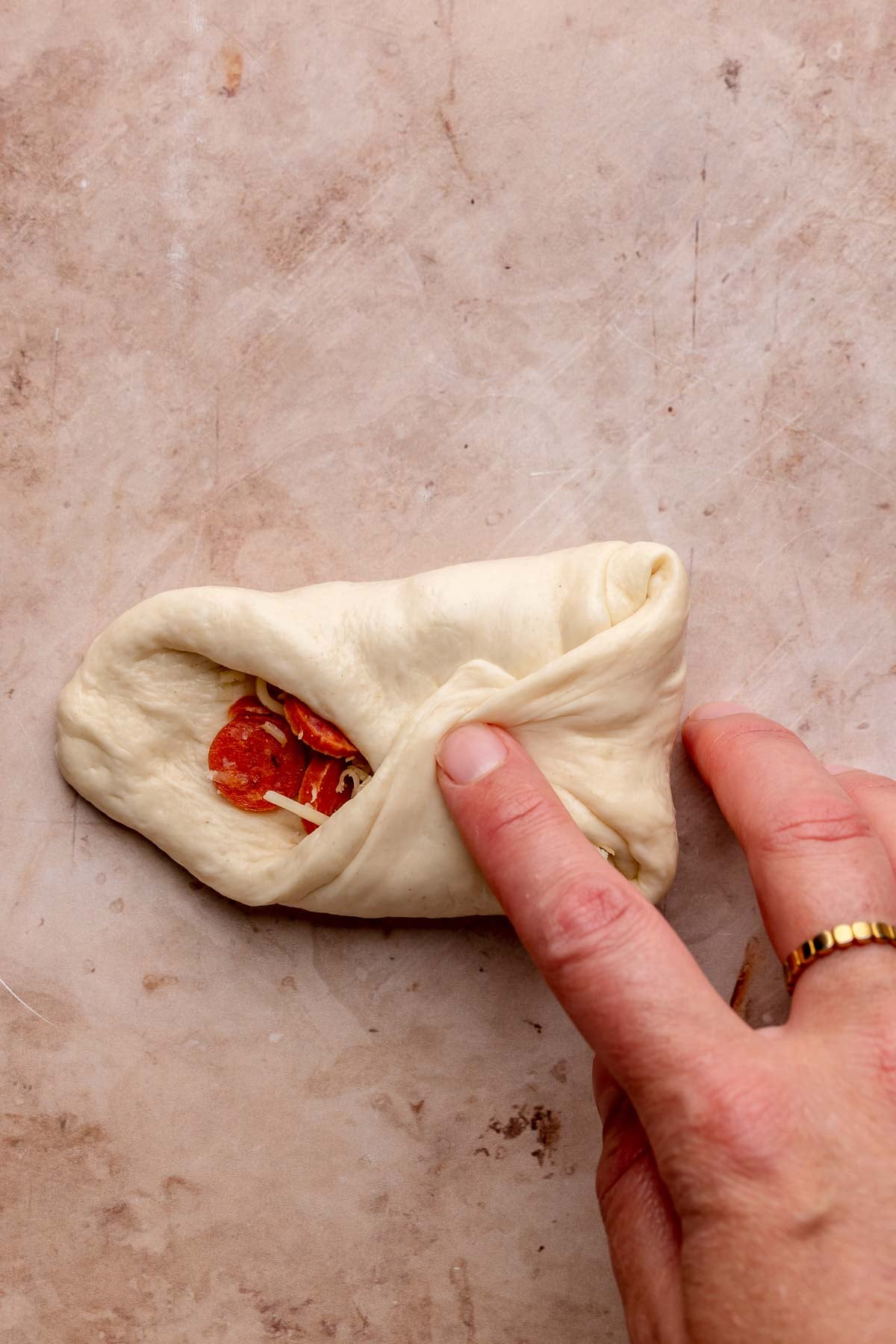 A hand folds sides of the dough around the cheese and pepperoni filling.
