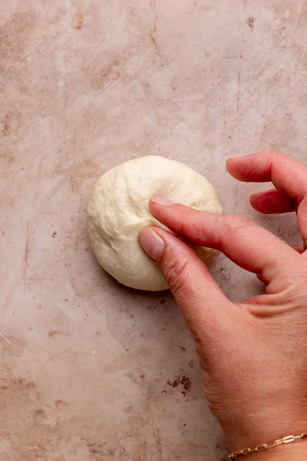 A hand pinches a dough ball closed.