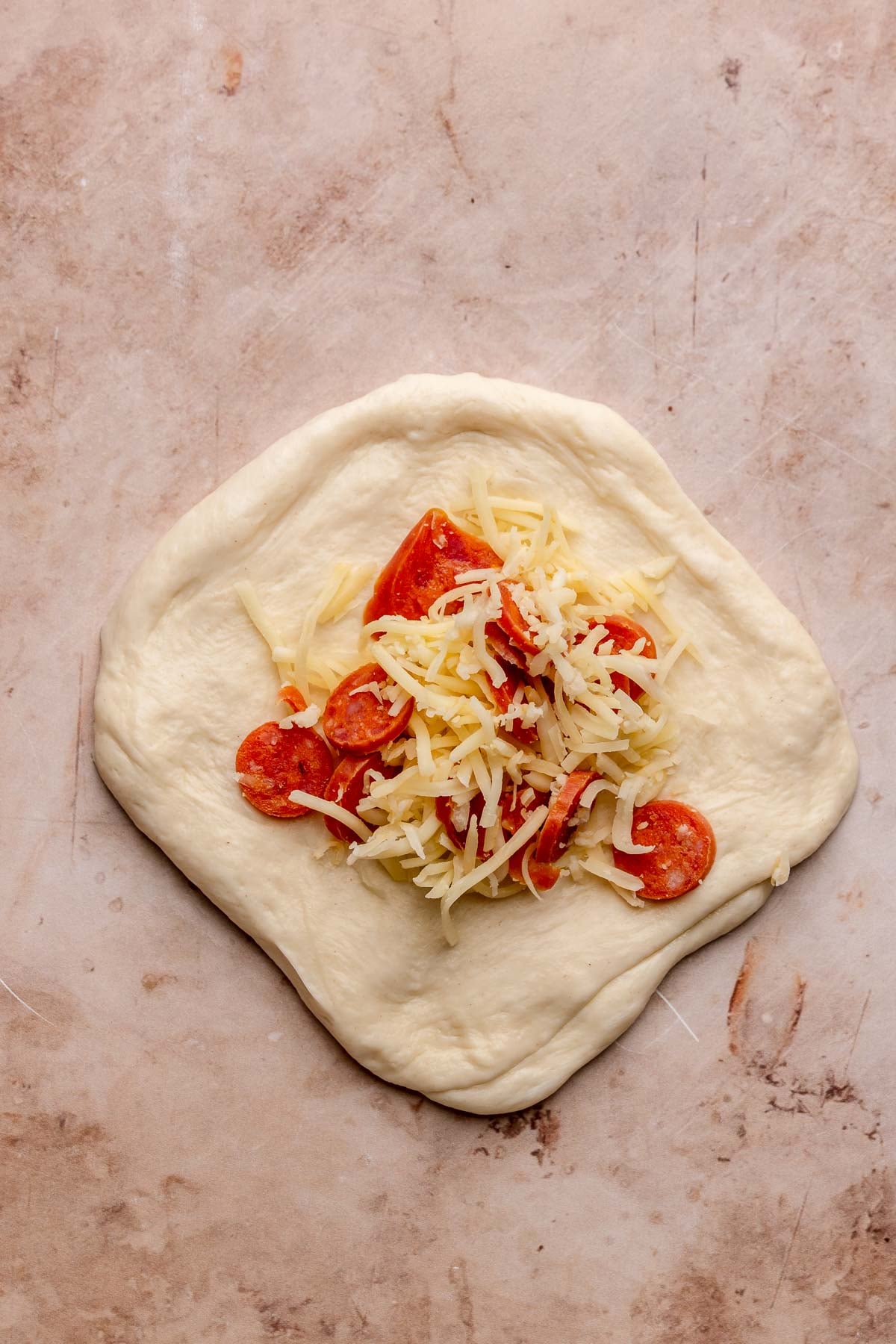 A flat round of pizza dough on the counter with a mound of cheese and pepperoni in the middle.