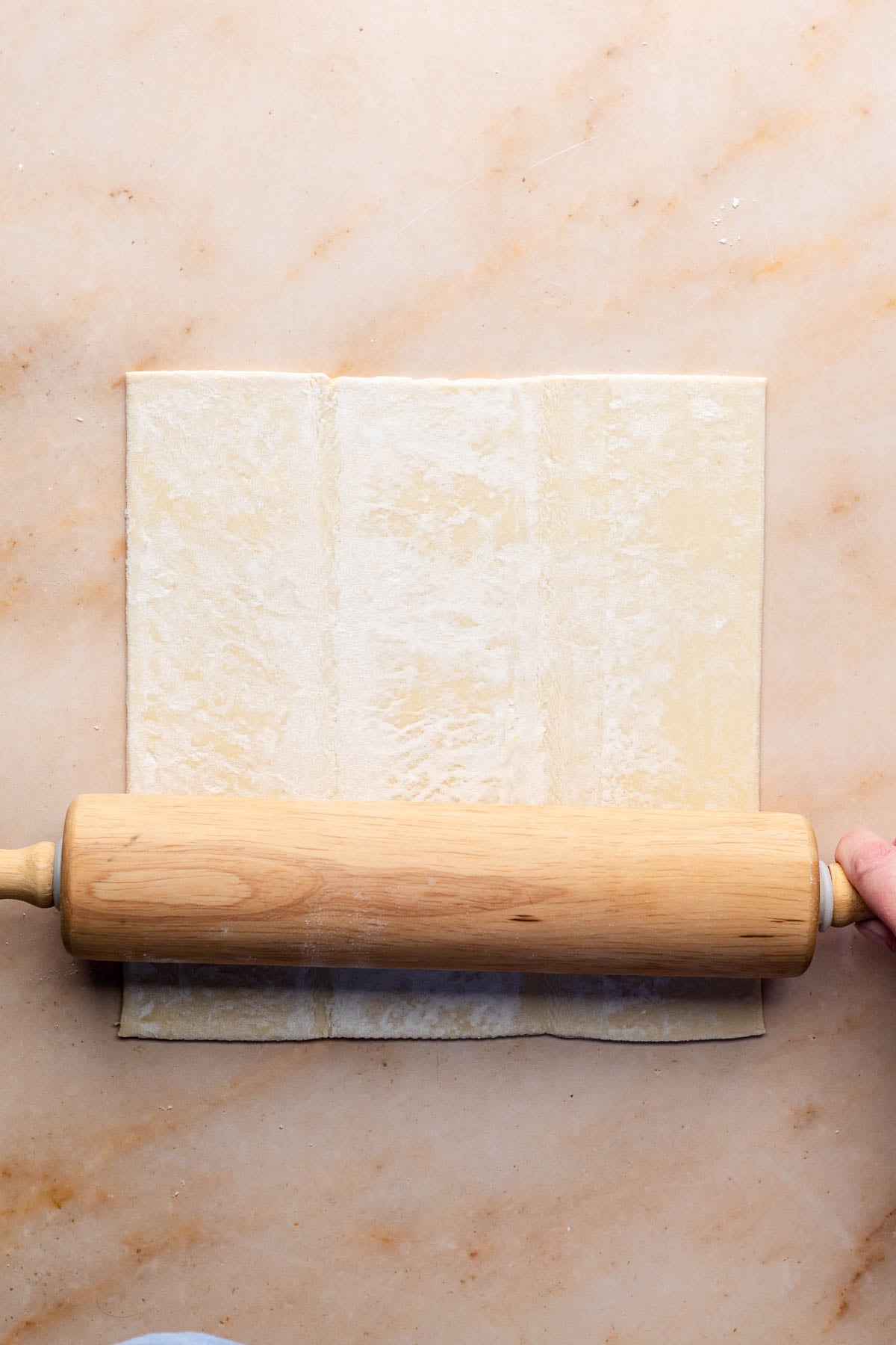 A rolling pin rolls a sheet of puff pastry.