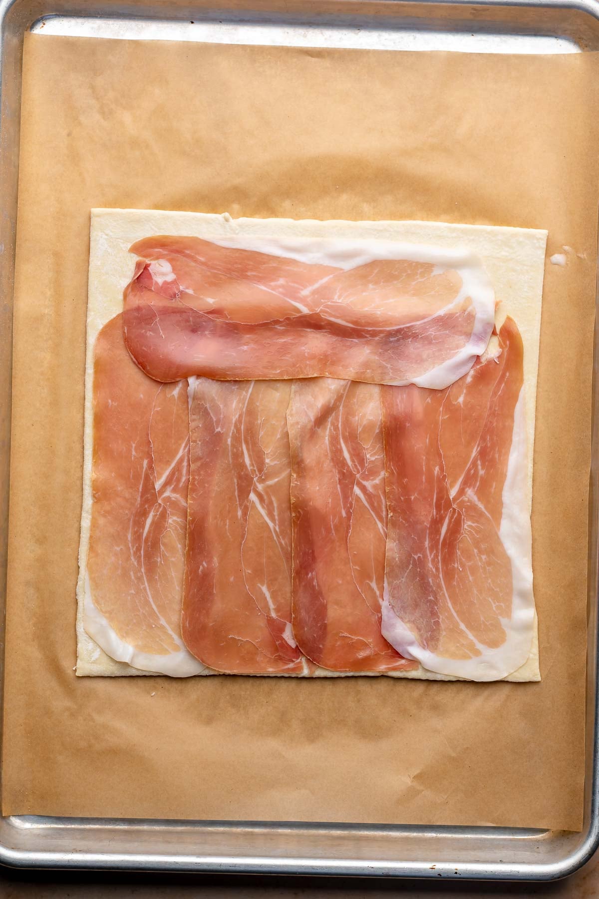Prosciutto slices layered onto a sheet of puff pastry.