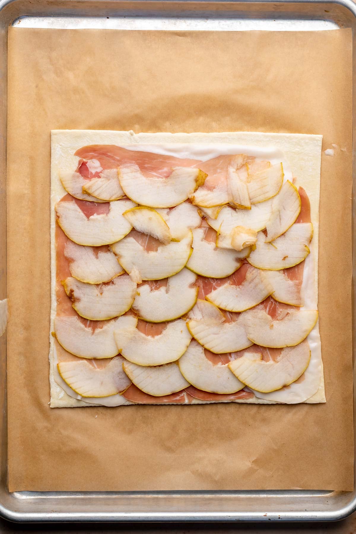 Pear slices lined up on top of the prosciutto and puff pastry.